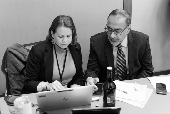 Program Director and planning committee member collaborating at a table while reviewing information on a laptop.